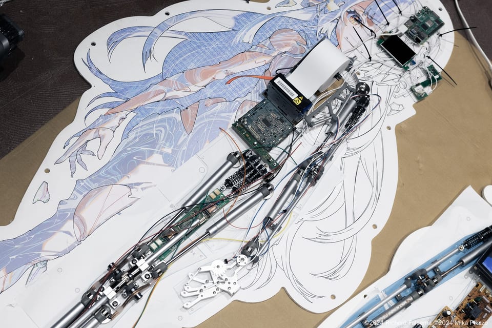 「グレイ」制作風景の俯瞰、内部の機構をイメージした骨組みがイラストパネルの上に配置される